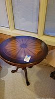 Full top view of round wood side table showing the sunburst pattern on the tabletop and label on the surface.