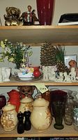 Shelf showing ceramic jars with lids, brass teddy bear figurines, artificial flowers, and Snow Babies figurines in cream porcelain.