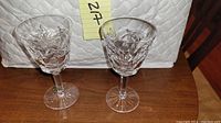 Two Waterford crystal wine glasses showing intricate cut patterns, standing about 6 inches tall on a wood surface.