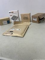 Photo showing multiple new electronic accessories including a Next-Shine digital scale box, digital clock, and several unopened packages.