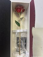 Gold dipped rose with red petals and green leaves displayed in original box with protective plastic wrap and acrylic stand