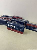 Photo showing six boxes of Honeywell Uvex safety eyewear in original packaging on a beige surface.