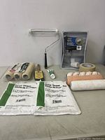 Wide shot of all painting supplies including roller, tray, drop sheets, tape, sanding block, and paint attachments.