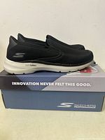 Side profile of black Skechers Go Walk men's shoes on top of the Skechers Performance shoebox