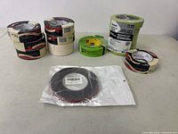 Wide view of multiple tape rolls including white masking tape, green electrical tape, black electrical tape sealed in bag, and a 6-roll pack of green Scotch masking tape.