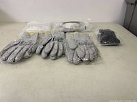 Photo of six pairs of grey cut-resistant work gloves with yellow trim and three pairs of clear safety glasses in packaging.