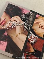 Close-up of the necklace coiled on a printed surface, shows chain texture and spring ring clasp.