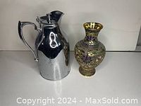 Front view of silver water jug next to gold floral decorative vase, showing size and design details