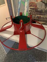 Top view of large red metal Christmas tree stand with three adjustable screws and green plastic interior holder.