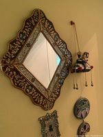 Front view of diamond shaped mirror showing floral print metal frame with scalloped edges and rose gold finish, hanging on wall next to hanging decorative pieces.