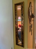 Full view of the narrow rectangular mirror hanging on a wall, showing the decorative metal frame and reflection of the room.