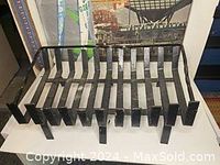 Front angle view of black metal fireplace tray showing heavy-duty slats and support legs