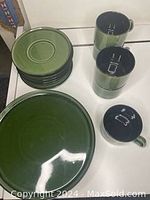 Overview of the dish set showing stacked plates, saucers, and cups with dark green and black glazing.