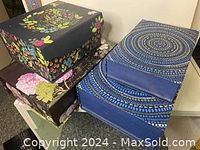 Four decorative gift boxes stacked, showing two dark blue floral and butterfly design boxes on the left and two blue circular patterned boxes on the right.