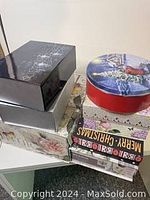 Stack of seven decorative gift boxes including black glossy boxes with floral design, a red round holiday box, and several rectangular floral and holiday-themed boxes.