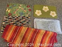 Five rugs and mats laid out including floral green mats, light blue shag rug, multicolored woven mat, and orange/red striped rug.