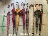 Eight umbrellas with varied colors and patterns laid out on tiled floor, showcasing diversity in handle style and fabric design.