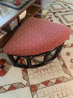 Triangular red floral fabric cushioned footstool on a wooden frame with visible paint chipping.