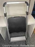 Front view showing folded step stool with ribbed black step and silver frame.