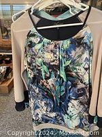 Photo of light beige long-sleeve top hanging with black cuffs and patterned short sleeve top with blue and green floral print.