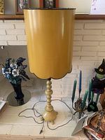 Full view of the tall yellow lamp with scalloped lampshade and turned base, showing the power cord on the floor.