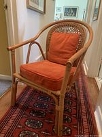 Side perspective of tan bamboo/wicker chair with orange cushions, showing frame and cushion detail.