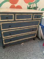 Front and angled view of vintage wooden chest of drawers painted blue with white trim, showing five drawers with black round handles and noticeable wear