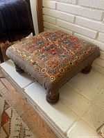Overall view of the square footstool showcasing the detailed orange and purple embroidery on the top and the brown fabric sides with nailhead trim.