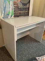 White wooden desk shown closed from front angle revealing smooth top and single open shelf below storage compartment.