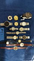 Photo of 13 wristwatches including metal and leather bands, various dial styles and colors on a blue background.