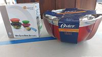 Photo showing boxed 10-piece glass bowl set with colorful lids and boxed 3-piece Oster stainless steel bowl set.