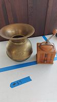 Photo of brass spittoon and wooden coffee grinder placed side by side