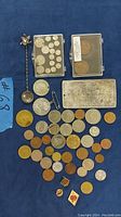 Full view of coins spread out on blue cloth, including the Tibetan Silver bar, spoon, medals, and pins