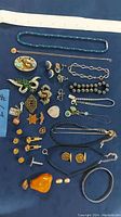 Full view of mixed costume jewelry on dark cloth including necklaces, brooches, earrings, bracelets, pendants, and cufflinks.