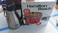 Hamilton Beach slow cooker in box shown together with Oster electric kettle on table