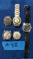 Full lot of 5 vintage men's watches on blue background showing various brands and strap styles.