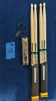 Photo showing set of three wooden Promark drumsticks, Echo harmonica, and metal mouth harp on dark blue background with seller lot number 76