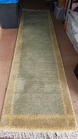 Full length top view of the Gabbeh runner rug, showing the green central field bordered in yellow-beige and white fringes.