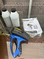 Photo of the blue and black Mastercraft spot sandblaster gun, two white bottles of sand media, and the instruction manual on a reflective surface.