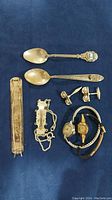 Lot showing two sterling spoons, cufflinks, barrette, bottle marker, and two wristwatches arranged on a dark blue surface.