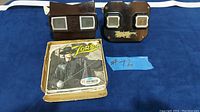 View of two vintage View-Master stereoscopic viewers, one brown and one black, alongside a box containing Zorro View-Master reels and sleeves.