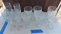 Front view of 10 crystal wine glasses, 5 tall champagne flutes and 5 shorter goblets, arranged in two rows with visible vertical cut design on clear glass.