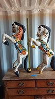 Two colorful Mexican wooden horses standing on hind legs placed on a wooden cabinet with measuring tape showing height