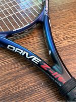 Close-up of tennis racket throat showing 'Drive Z Lite' branding and carbon composite frame details.