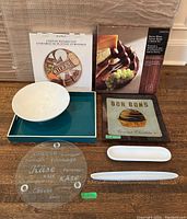 Photo showing assortment of serving items including white bowl, acrylic cheese board, Bon Bons plate, and utensils along with packaged sets