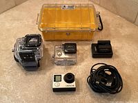 Full lot view with GoPro camera, two housings, Pelican case, charging dock, and USB cable.
