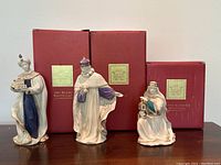 The lot shows three Lenox nativity scene wise men figurines next to their original red boxes. The tallest figure is on the left standing 9 inches tall. All figures are porcelain with white, blue, and gold coloring.