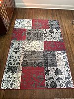 Full view of the rectangular area rug on wood flooring showing the patchwork floral pattern in red, gray, black, and white blocks.