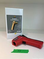 Red handheld infrared thermometer beside white box with product label 'IR-GUN-S Infrared Thermometer'