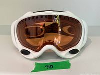 Front view of white Oakley ski goggles with amber lens and ventilation holes along top.